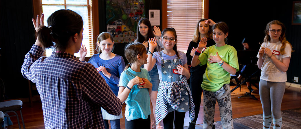 Middle school aged students raising hands and participating with a teacher