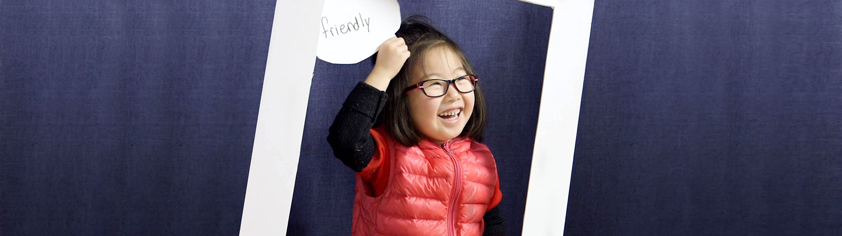 Child smiling and holding up a card with the word "friendly"