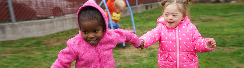 Two kids are running around outdoors on the grass.