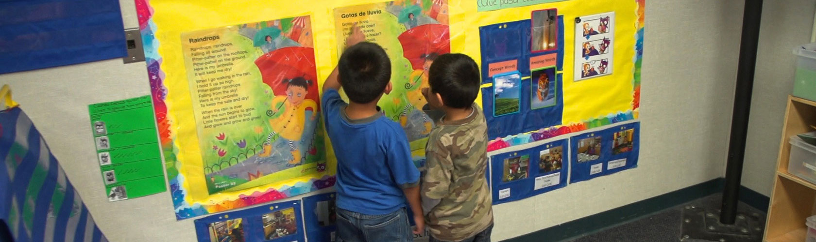 Two preschoolers looking at a colorful poster on the wall.